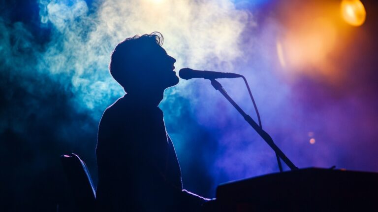 Silhouette of a male singer performing at a microphone, outlined against vibrant blue and purple stage lights with a smoky atmosphere in the background, capturing a dramatic and intense live music scene.